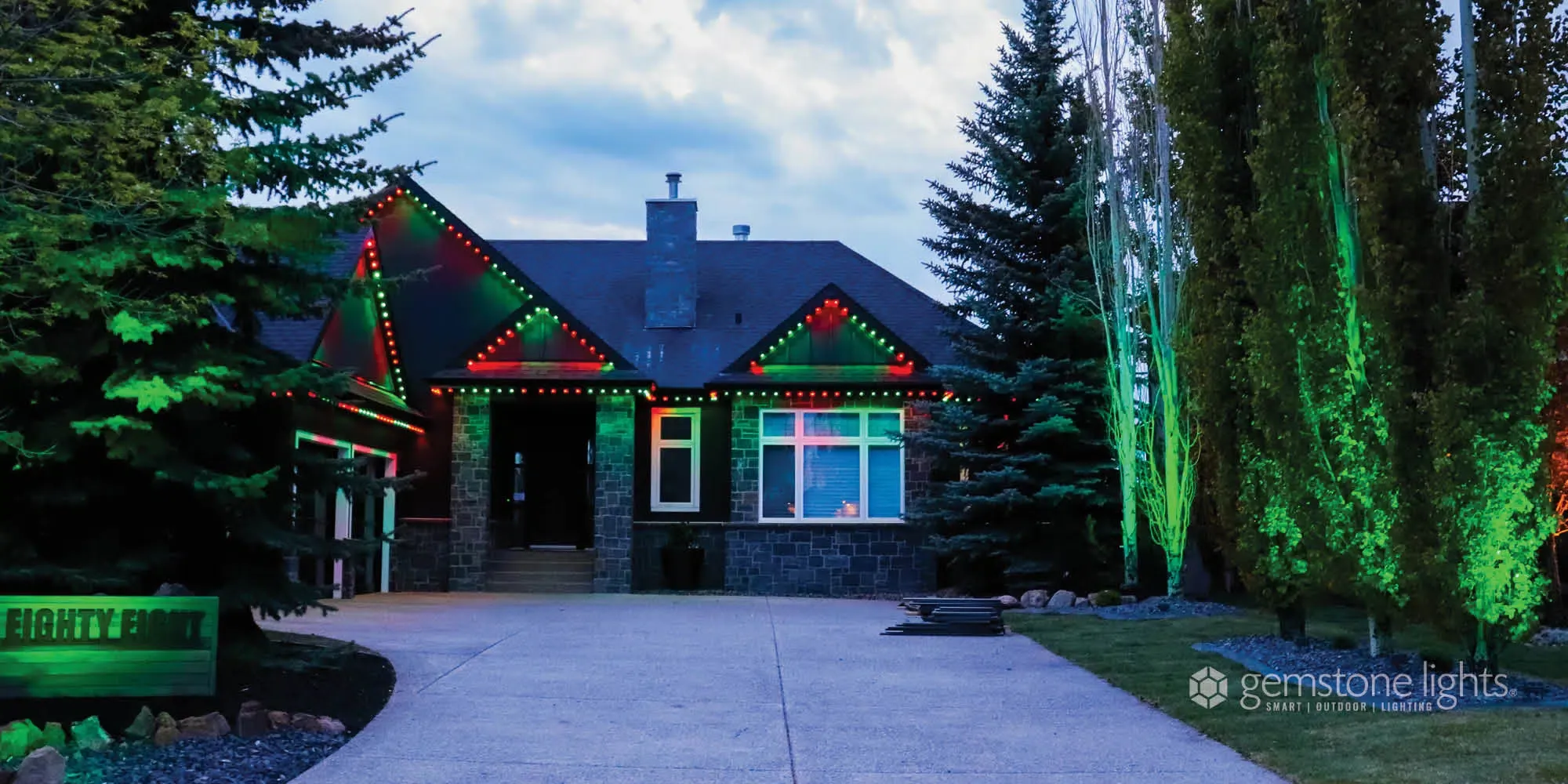 Bungalow with trees lit green along the driveway