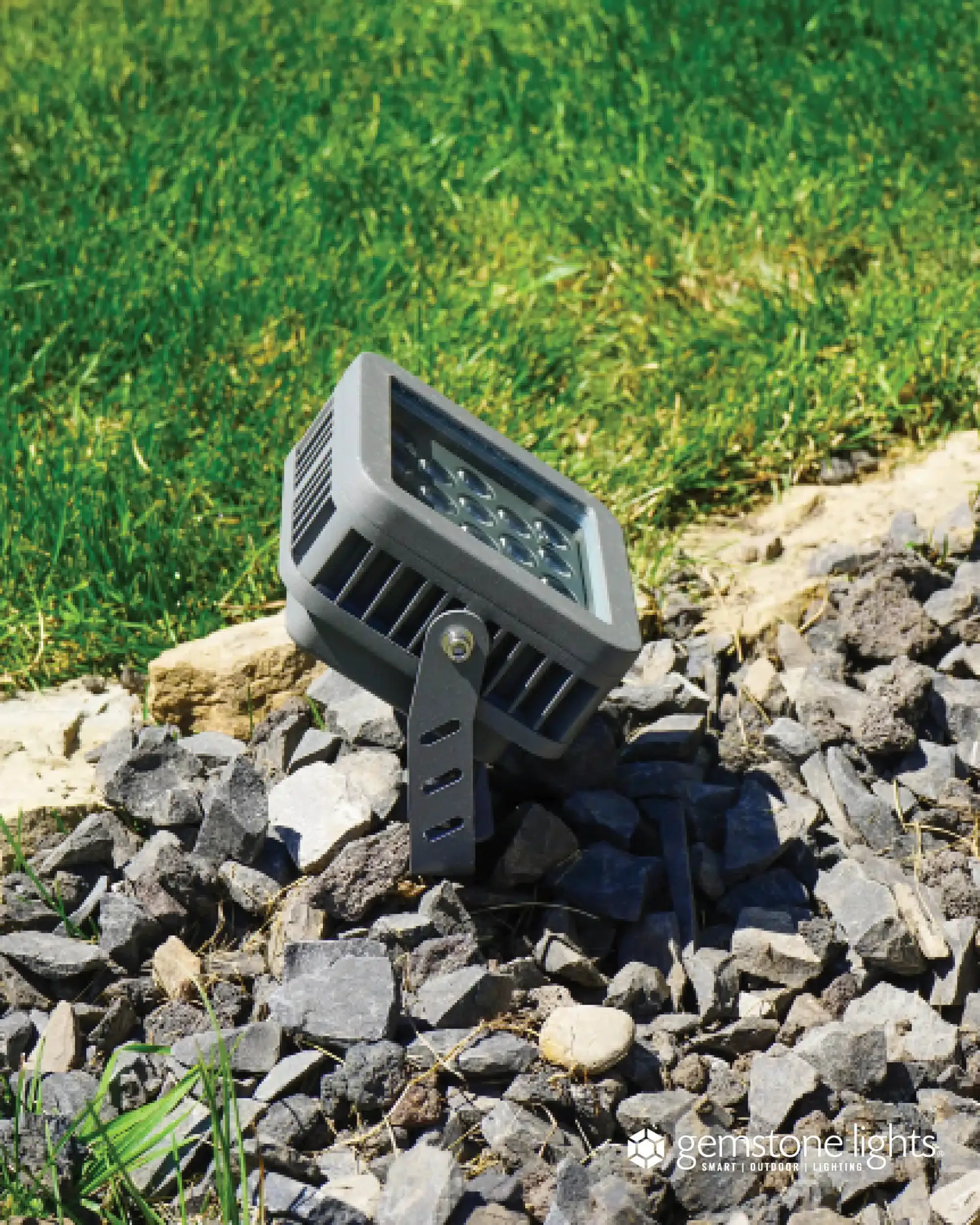 Gemstone flood light, a square grey fixture with a grid of LEDs, staked among landscape rocks