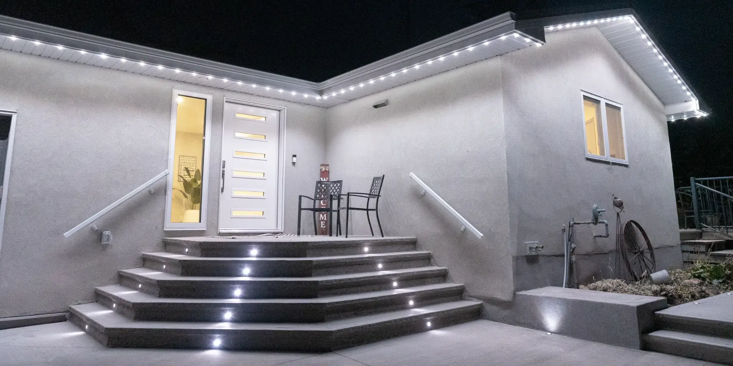 Stucco house at night with white roofline lights and lights in the front steps