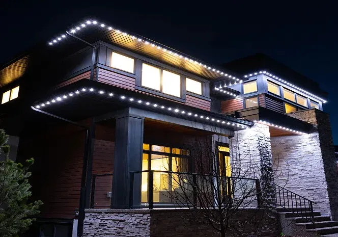 Modern house at dusk with white lights along the rooflines and warm light in the windows