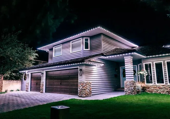 House with white lights along every roofline above a double garage with stone pillars