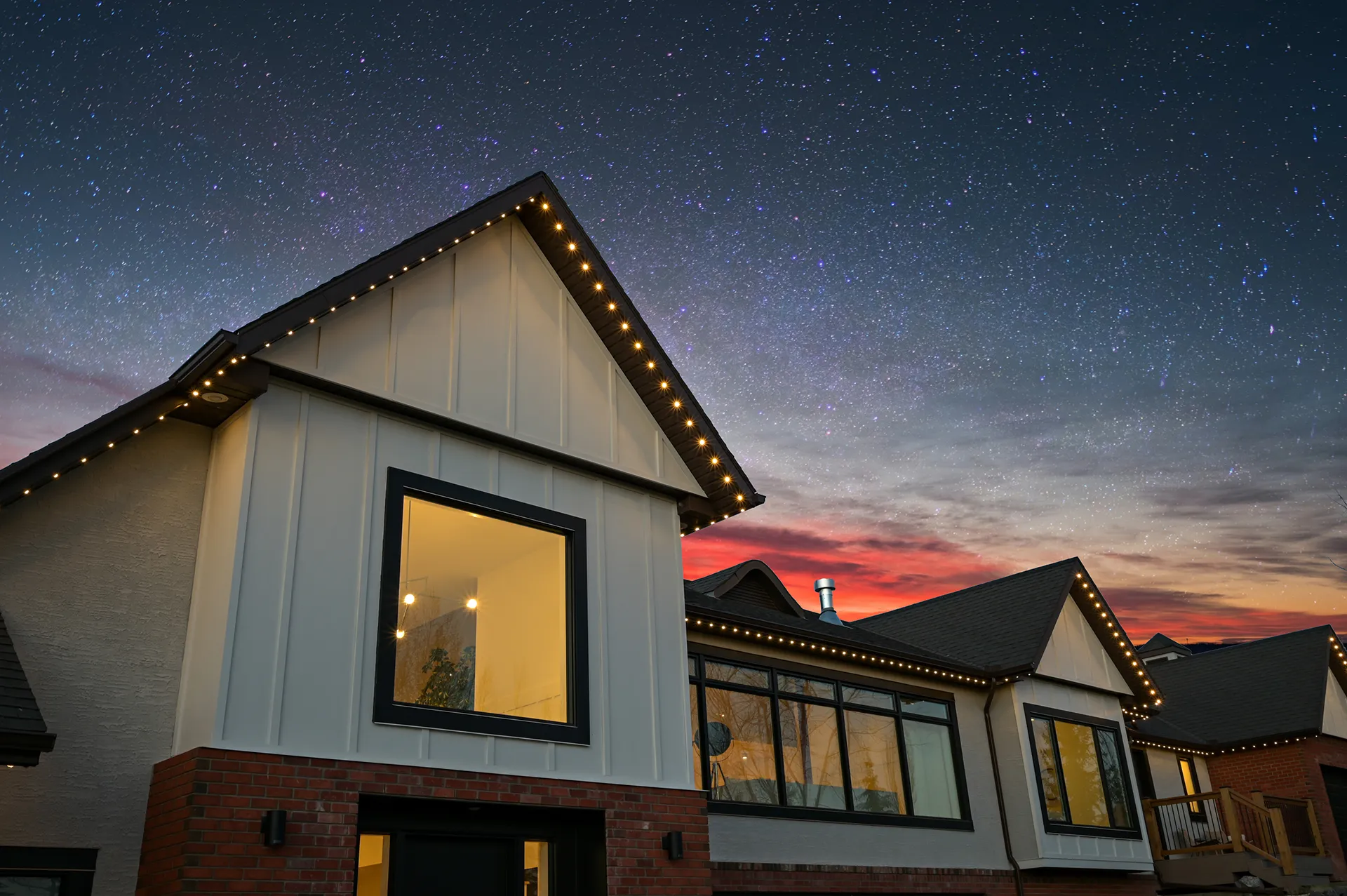 Modern farmhouse gables in warm white under a starry sky with a red sunset glow