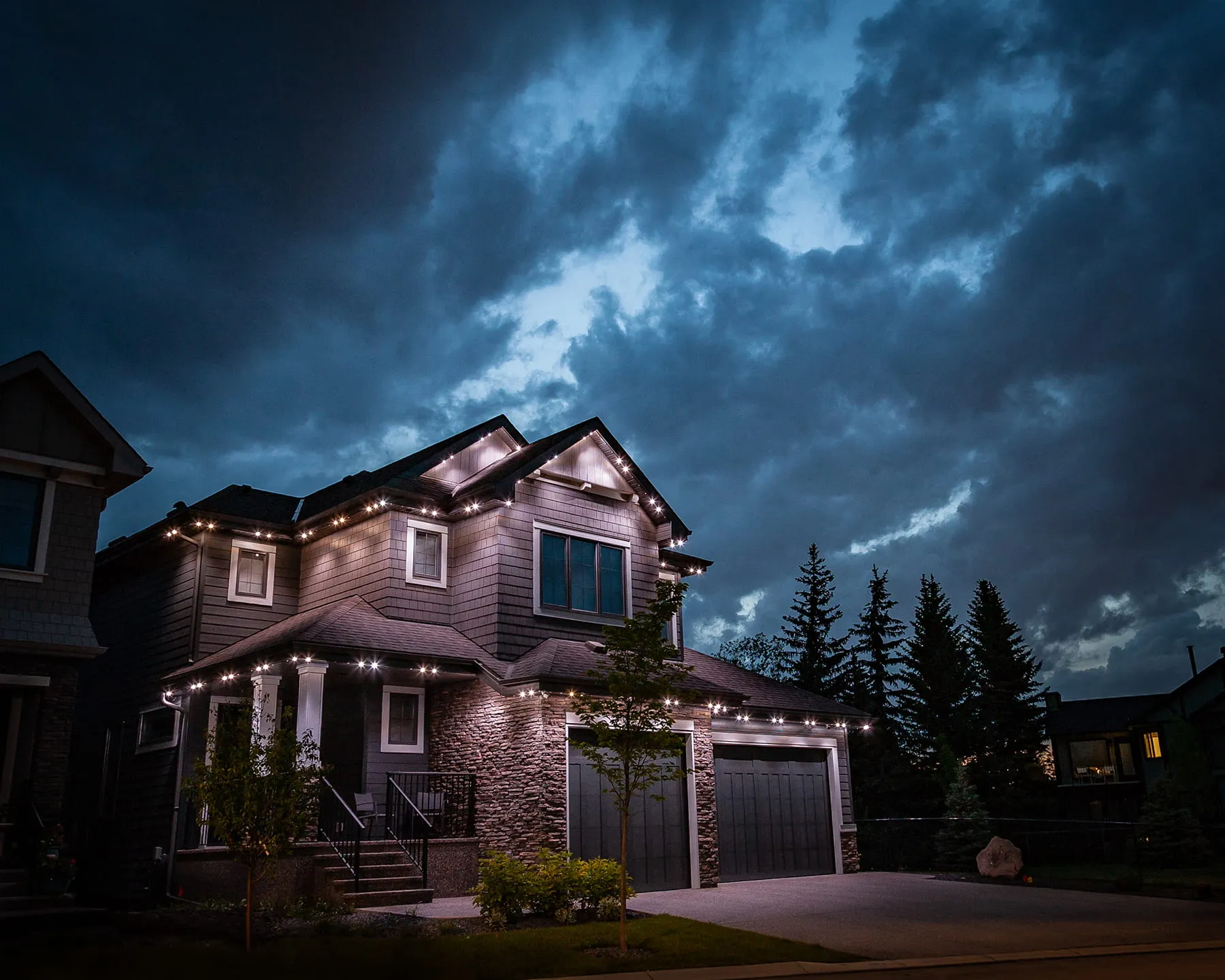 Two-storey house with bright white lights along every roofline under a stormy sky