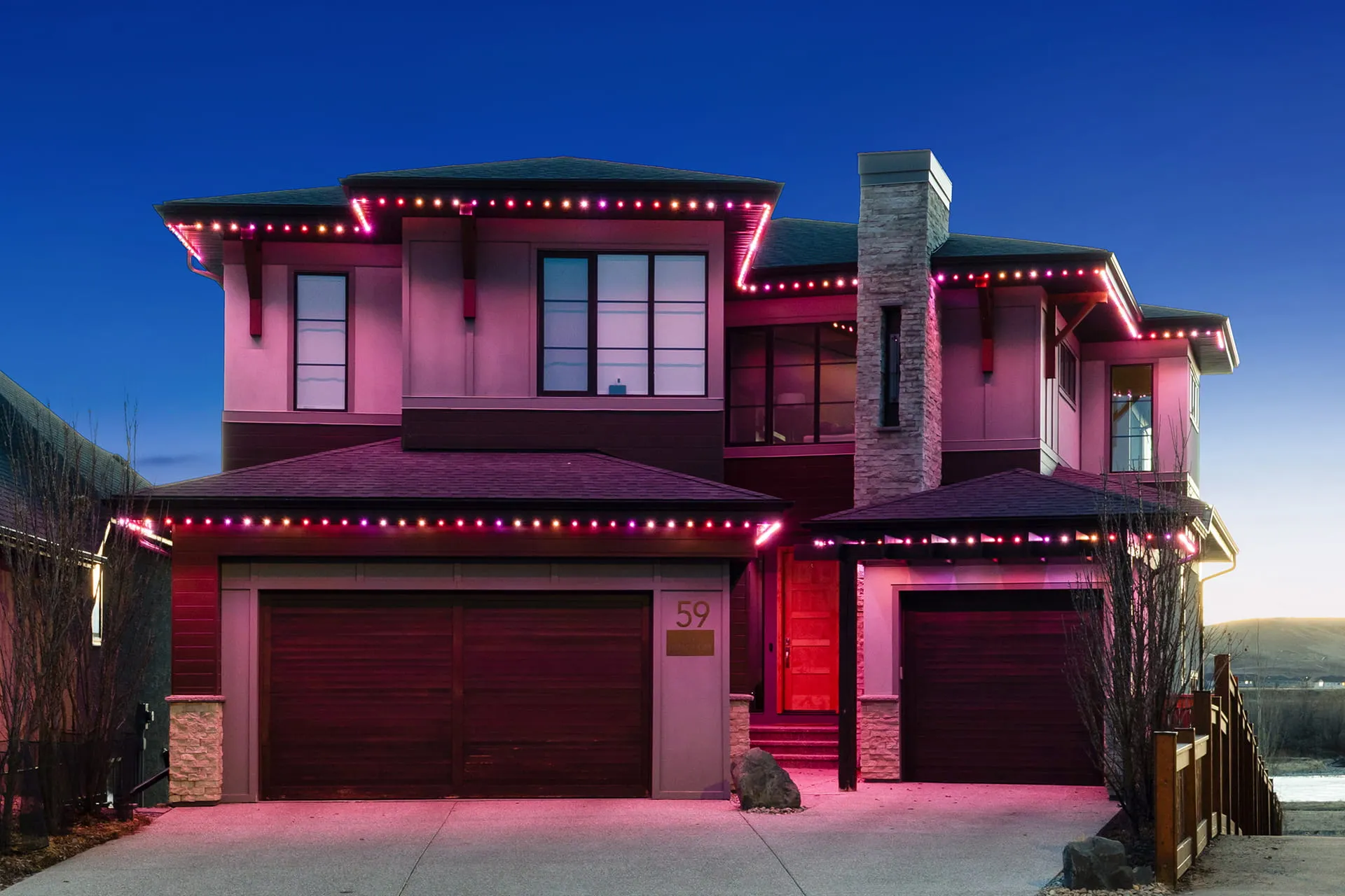 Two-storey house with pink and red roofline lights at blue hour